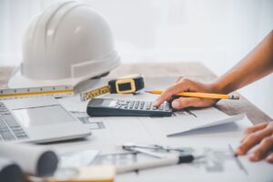 desktop with papers, calculator and hardhat tabulating construction overhead