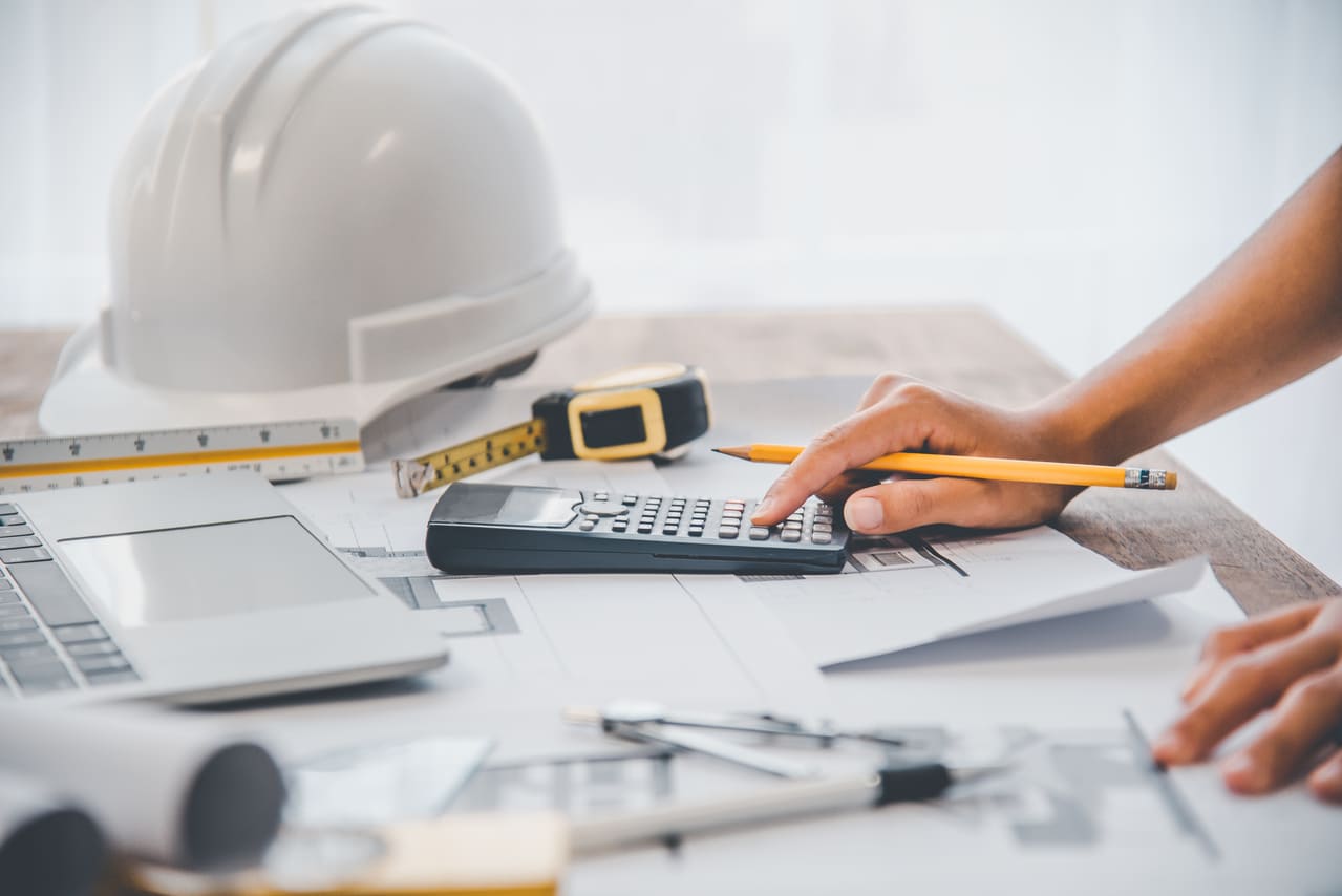 desktop with papers, calculator and hardhat tabulating construction overhead